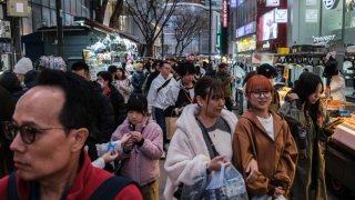 Pedestrians walk past food stalls and shops in the Myeongdong shopping district of Seoul on March 26, 2024.