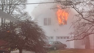 Flames pouring from the window of an apartment over a garage in Biddeford, Maine, on Monday, Dec. 30, 2024. A man was pulled from the fire and later died.