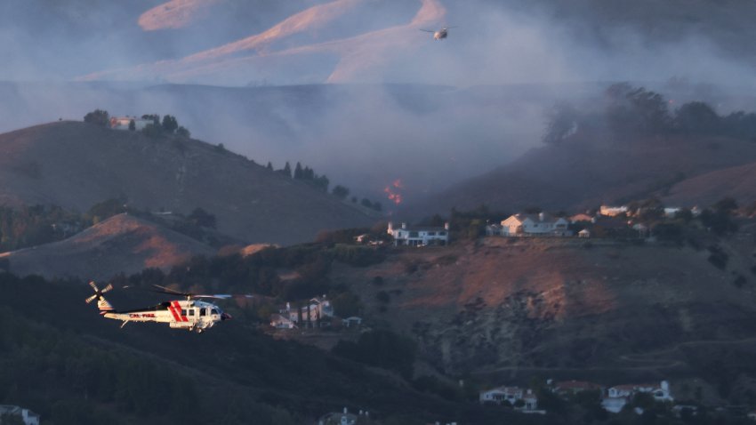 A CalFire helicopter flies near plumes of smoke